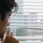 Man looking out window blinds